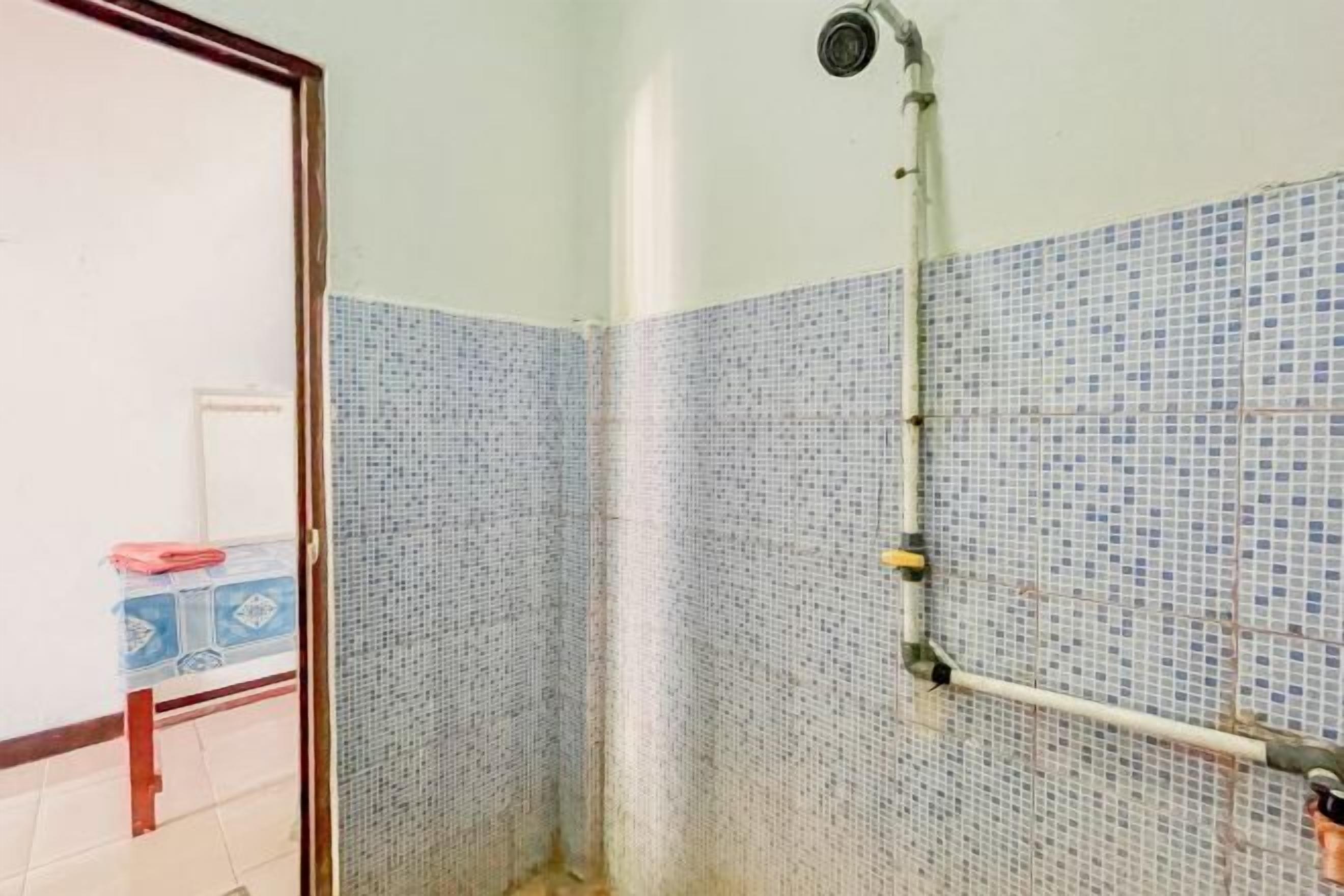 Un baño con ducha, paredes de azulejos y una tubería visible.