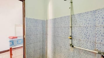 Un baño con ducha, paredes de azulejos y una tubería visible.