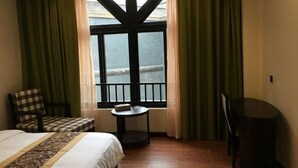 A hotel room with a bed, a small table, a chair, and a view of the sea through a window with black frames. - Colorful Royal Hotel (Qingzhen Time Guizhou Ancient Town) (Qingzhen)