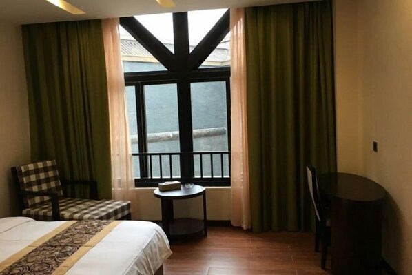 A hotel room with a bed, a small table, a chair, and a view of the sea through a window with black frames. - Colorful Royal Hotel (Qingzhen Time Guizhou Ancient Town) (Qingzhen)