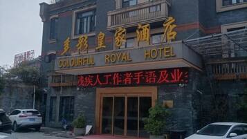 Entrada de um hotel com uma placa que diz 'Colourful Royal Hotel' e uma placa menor abaixo com a inscrição 'Warrior Writer's Handwriting & Business'.