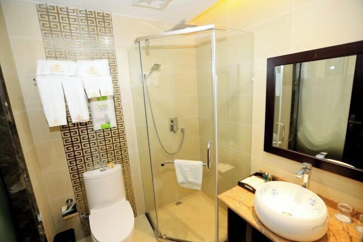 A bathroom with a glass-enclosed shower, a white toilet, a marble sink, and a mirror above the sink.