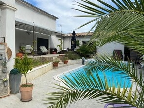 Ein Poolbereich mit Terrasse, Blumentöpfen und Gartenmöbeln.