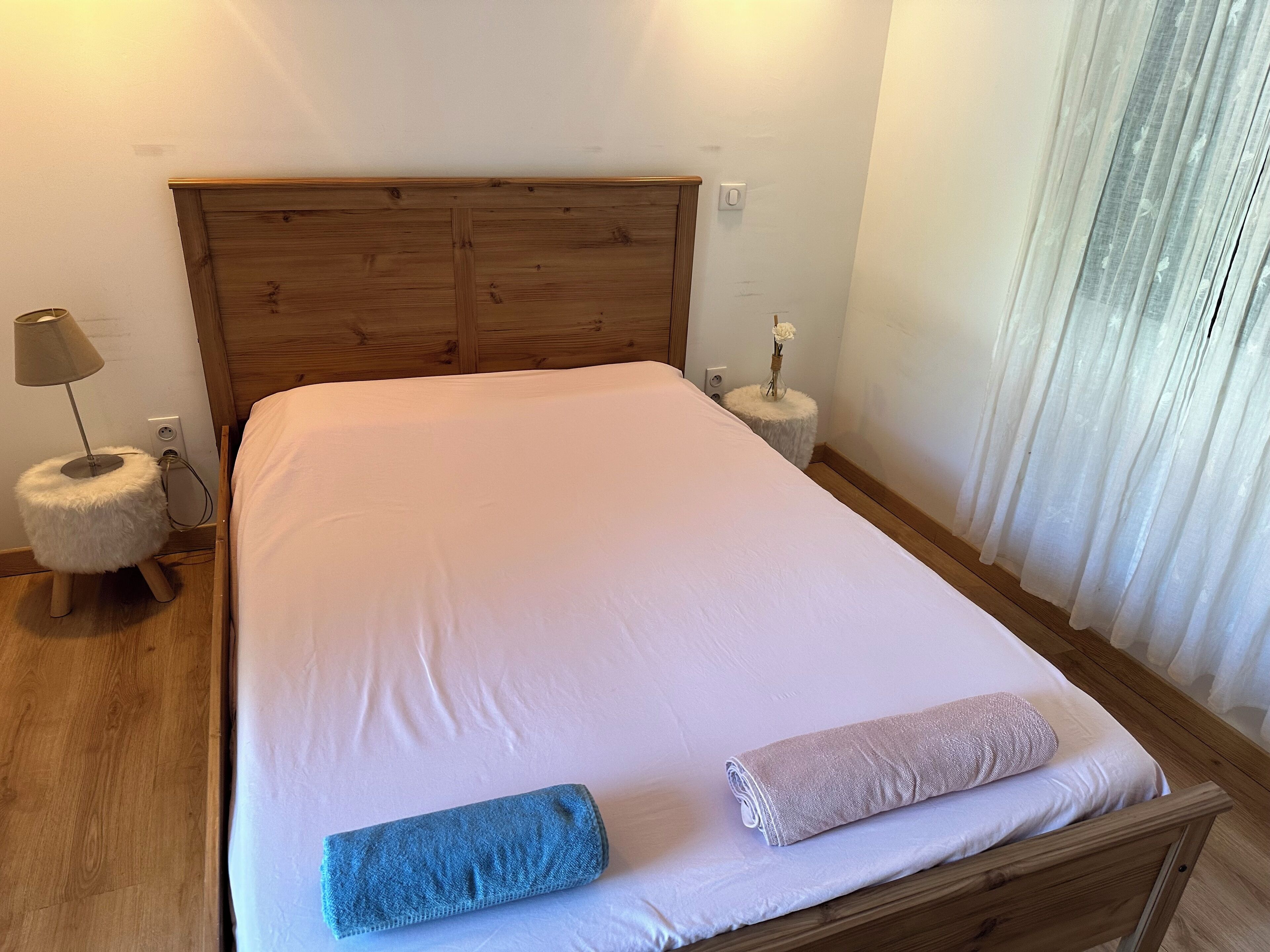 A neatly made bed with a wooden headboard, a small bedside table with a lamp, and a fluffy white cushion.