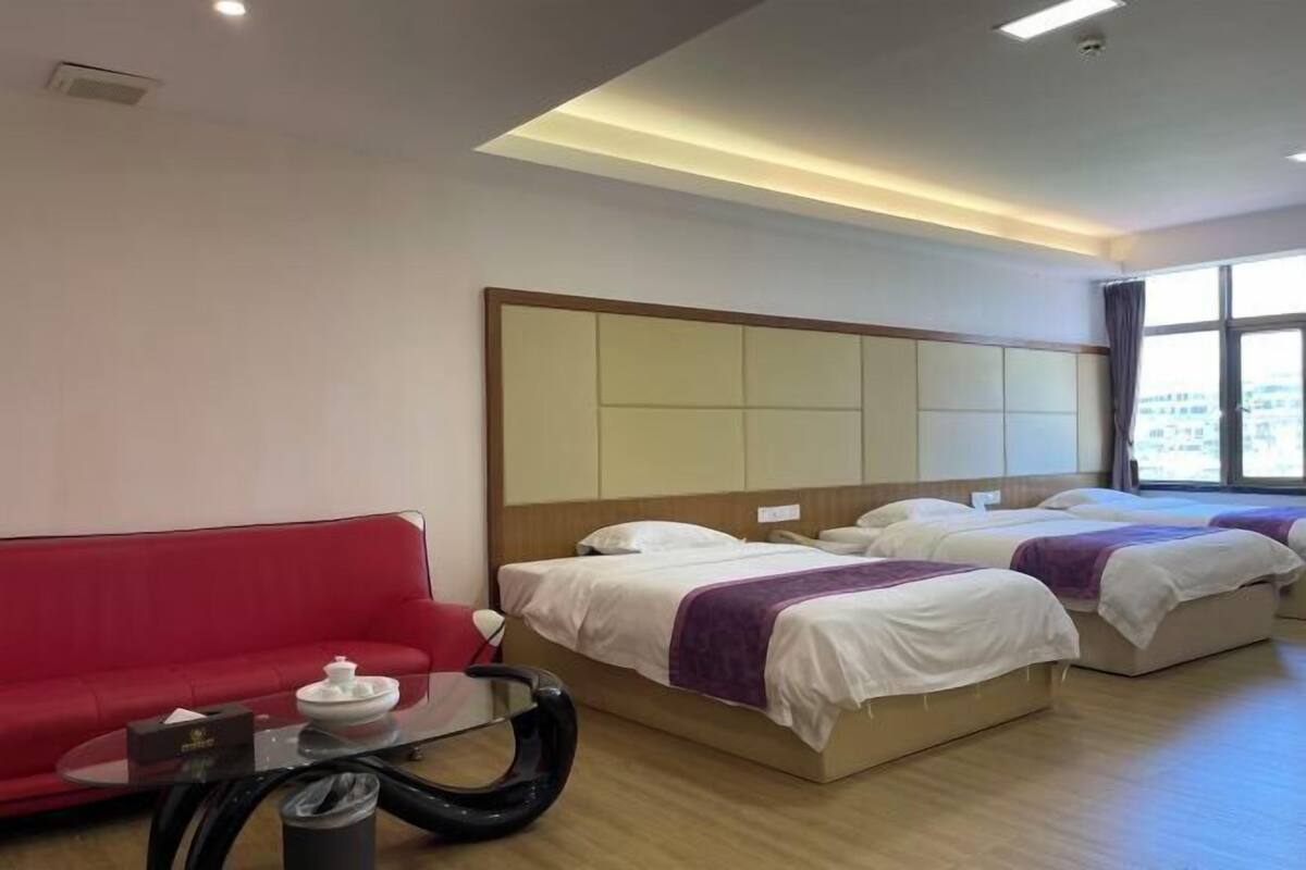 A hotel room with two beds, a red sofa, a glass coffee table, and a large window.