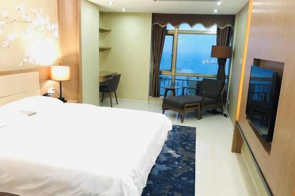 A hotel room with a large bed, a desk with a chair, a TV, and a balcony with a view.