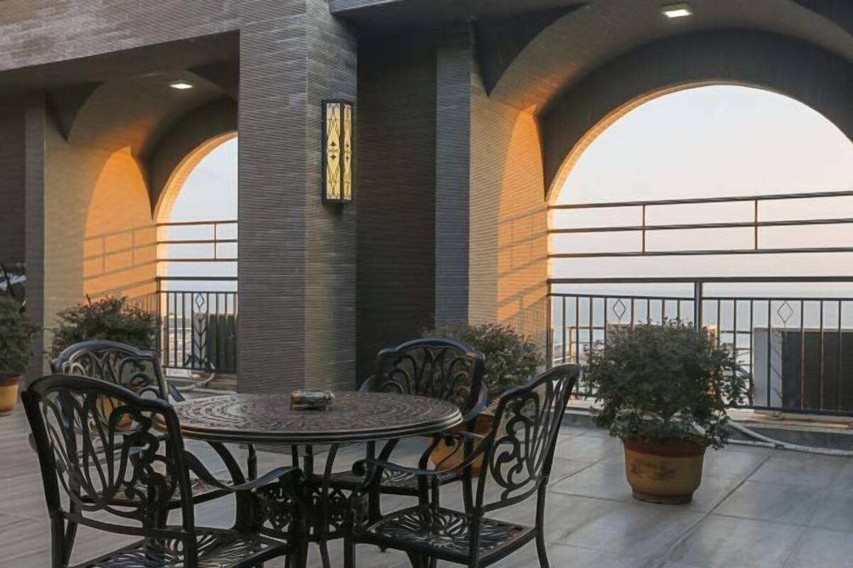 An outdoor patio with a round table and chairs, surrounded by potted plants and a brick wall.