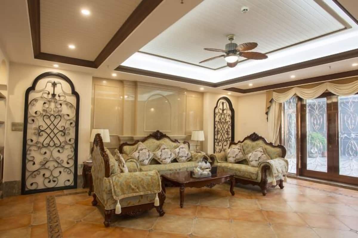 A spacious living room with a high ceiling, a ceiling fan, and a large window with curtains.