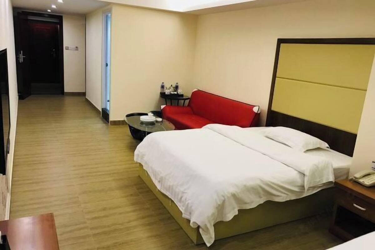 A hotel room with a bed, a red sofa, a small table, and a bedside table.