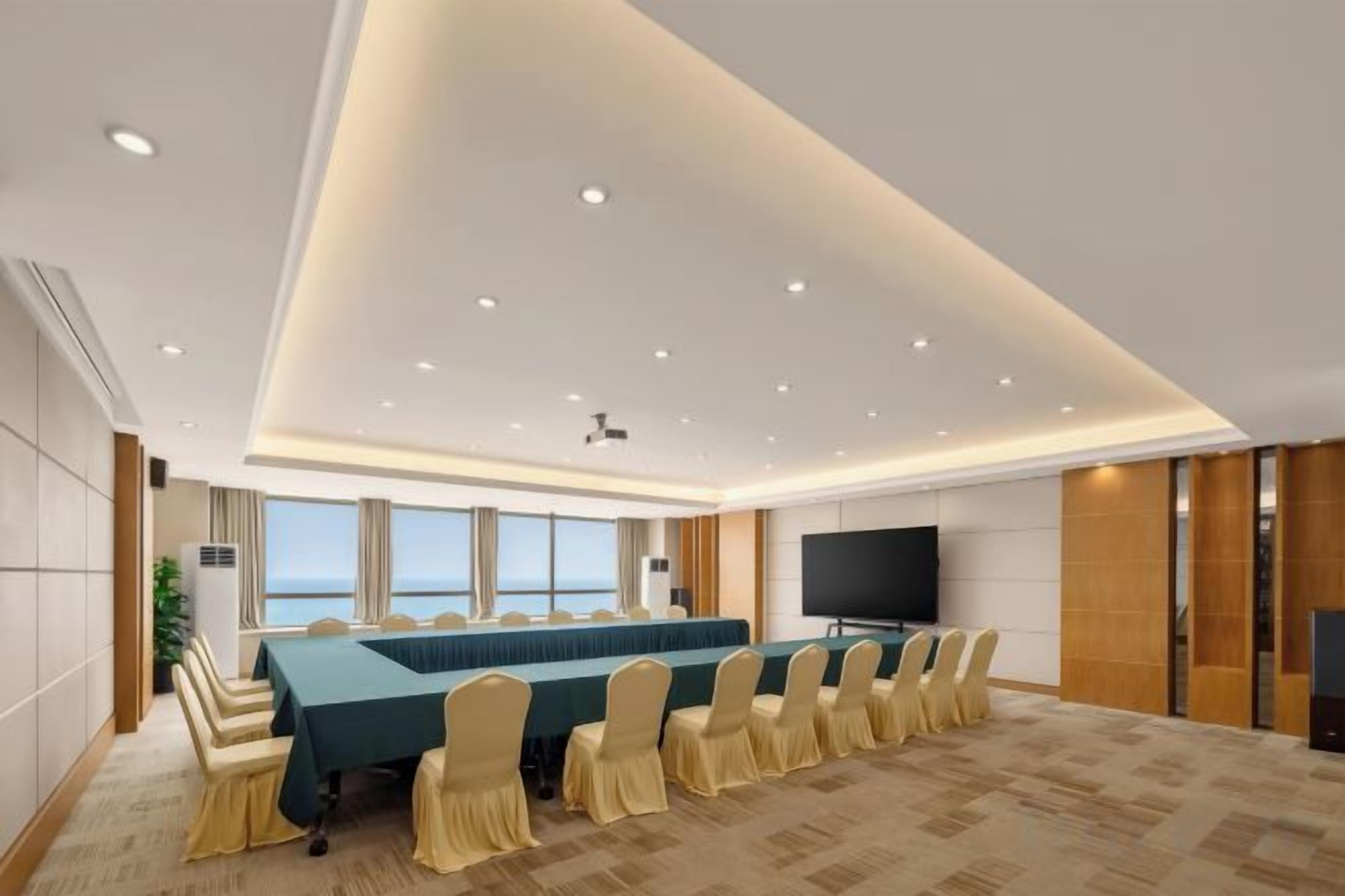 A conference room with a long table, chairs, a flat-screen TV, and a large window.