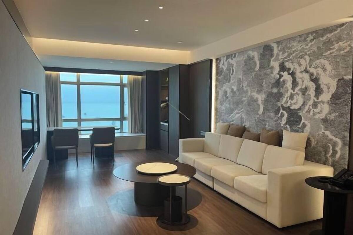 A modern living room with a sofa, two chairs, a coffee table, and a large window with a view.