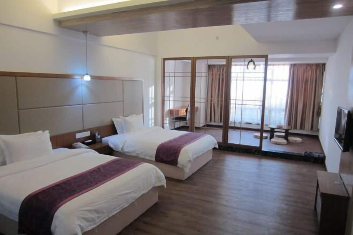 A hotel room with two beds, a wooden ceiling, a sliding glass door leading to a balcony, and a small table with chairs.