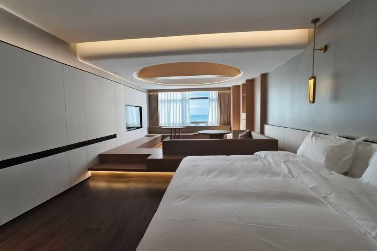A modern hotel room with a large bed, a seating area with a view, and a television.