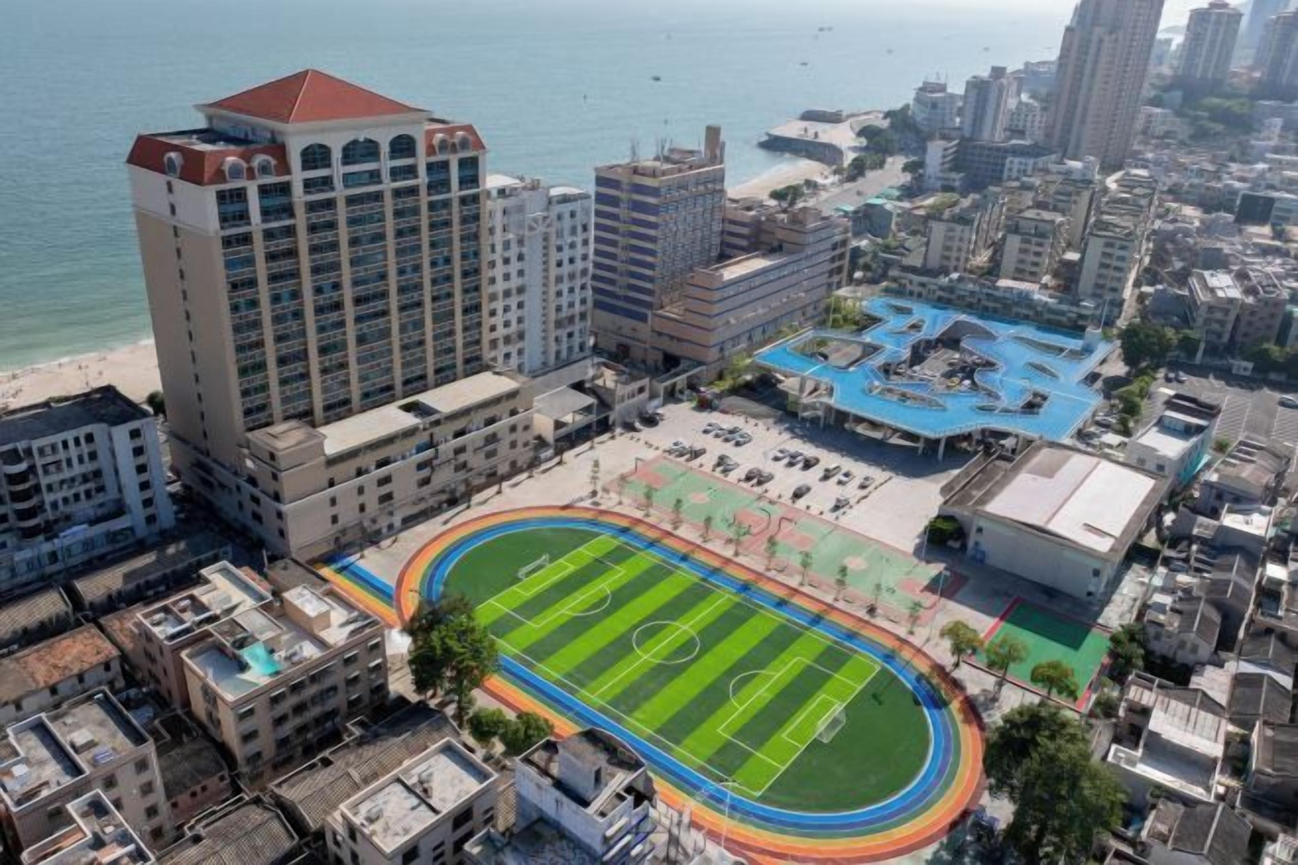 Une vue urbaine comprenant un grand immeuble, un terrain de sport et une étendue d’eau.