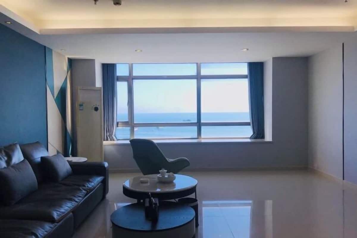 A modern living room with a leather sofa, a round coffee table, and a view of the sea through large windows.