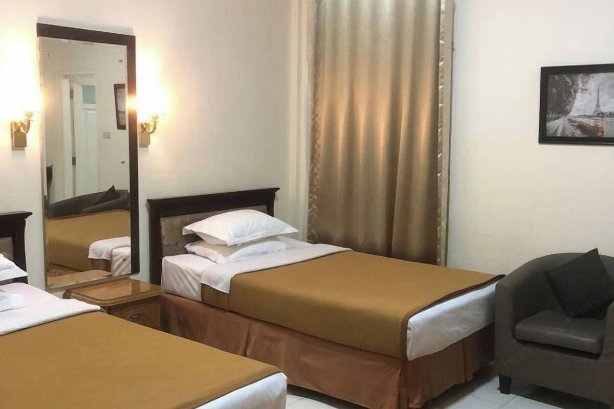 A hotel room with two beds, a chair, a mirror, and a painting on the wall.