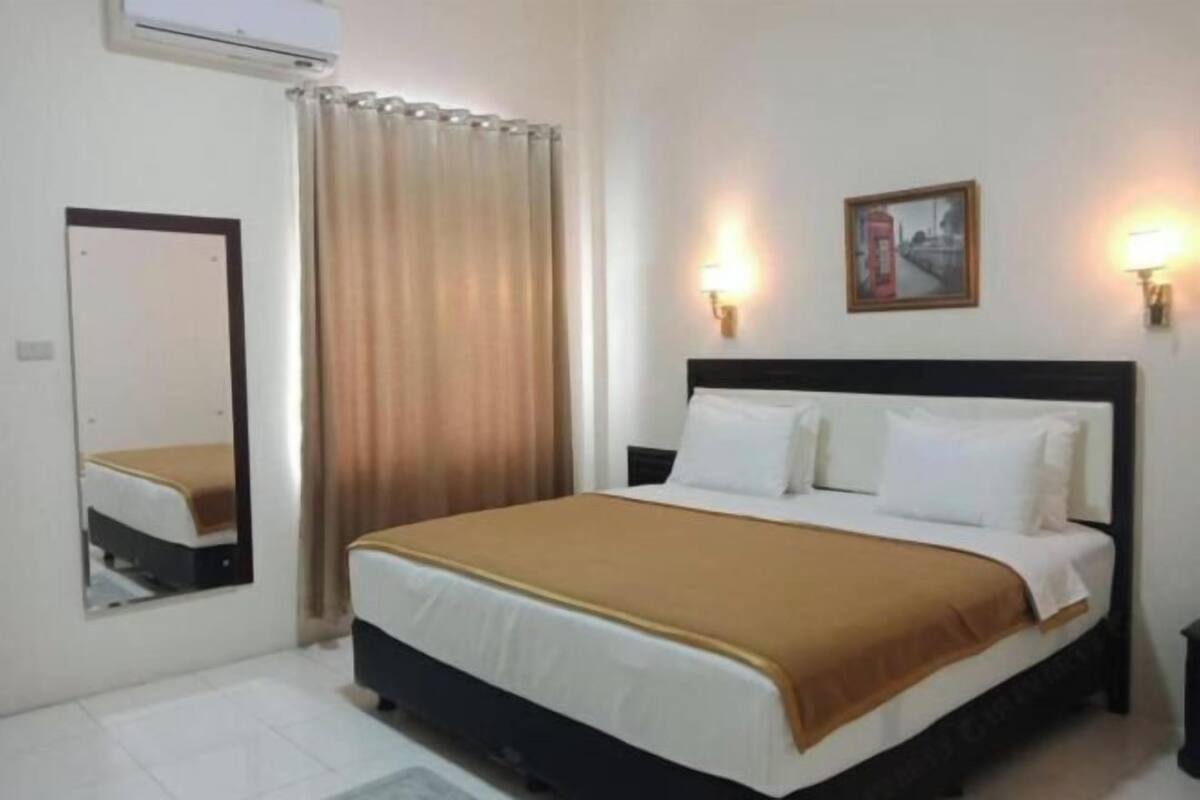 A hotel room with a bed, a mirror, a picture on the wall, and a window with curtains.