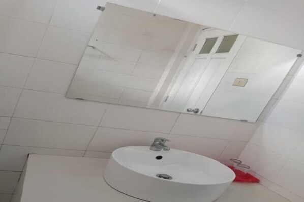 A bathroom with a white sink, a mirror, and a tiled wall. - Monika Hotel (Rantepao)