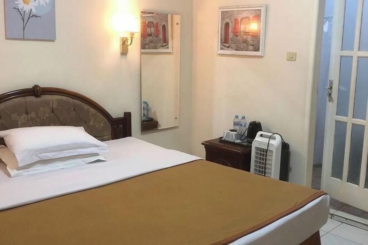 A hotel room with a bed, a bedside table with a phone and a water bottle, a mirror, and wall art.