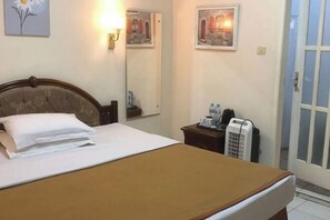 A hotel room with a bed, a bedside table with a phone and a water bottle, a mirror, and wall art. - Monika Hotel (Rantepao)
