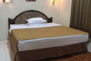 A neatly made bed with a brown headboard, white bedding, and a brown skirt. - Monika Hotel (Rantepao)