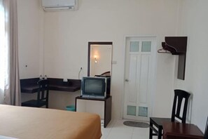 A hotel room with a bed, a desk with a television, a door, and a small table. - Monika Hotel (Rantepao)