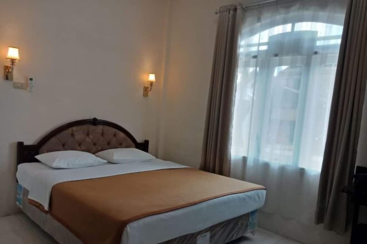 A hotel room with a bed, two wall-mounted lamps, and a window with curtains.