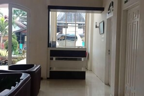 A hallway with a bench, a door, and a window with a view of a parked car and greenery outside. - Monika Hotel (Rantepao)