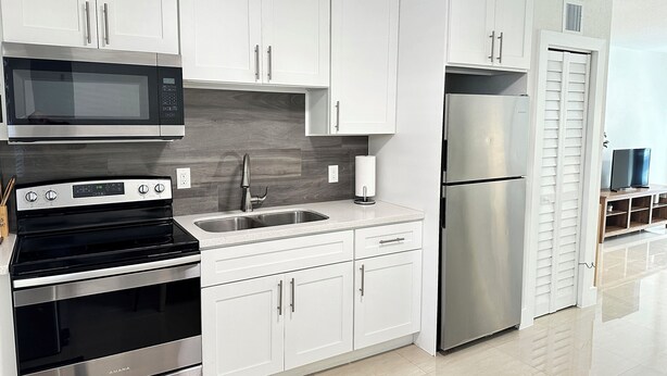 A modern kitchen with white cabinets, stainless steel appliances, and a tiled backsplash. - Miami Design District/ Wynwood Townhome 298 (MIAMI)