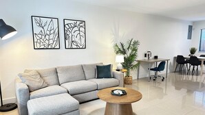 A modern living room with a grey sectional sofa, a round wooden coffee table, and two wall-mounted abstract art pieces. - Miami Design District/ Wynwood Townhome 298 (MIAMI)