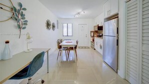 A modern kitchen with white cabinets, a stainless steel refrigerator, and a dining area with a table and chairs. - Miami Design District/ Wynwood Townhome 298 (MIAMI)