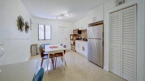 A modern kitchen with white cabinets, a stainless steel refrigerator, and a dining area with a white table and chairs. - Miami Design District/ Wynwood Townhome 298 (MIAMI)