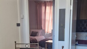 Una stanza con un tavolo da pranzo in vetro, due sedie, un letto con copripiumino rosa e una televisione in un'altra stanza.