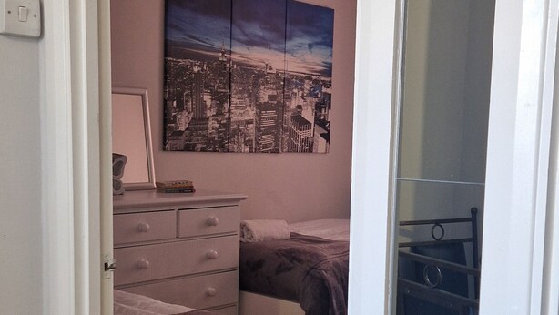 Una camera da letto con un letto, una cassettiera, un comodino e un dipinto con vista sulla città.