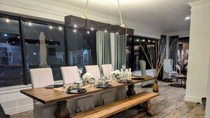 Un coin repas avec une longue table en bois, dressée pour six personnes, entourée de chaises, et un banc à l’extrémité.