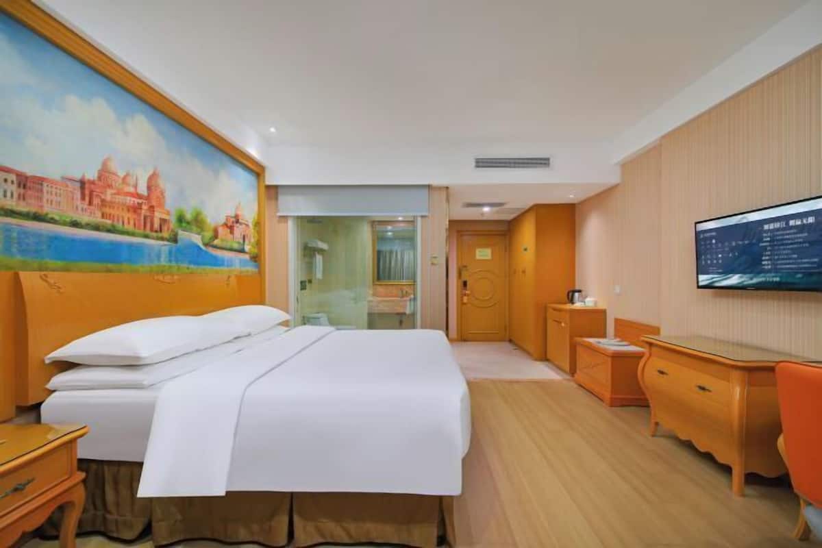 Habitación de hotel con cama, escritorio, silla, televisión y un cuadro en la pared.