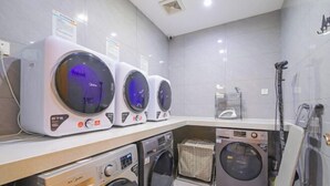 A laundry facility with multiple washing machines and dryers, a tiled wall, and a ceiling vent. - Vienna Hotel (Suzhou Industrial Park, Yangcheng Lake, Fashion Stage) (Suzhou)
