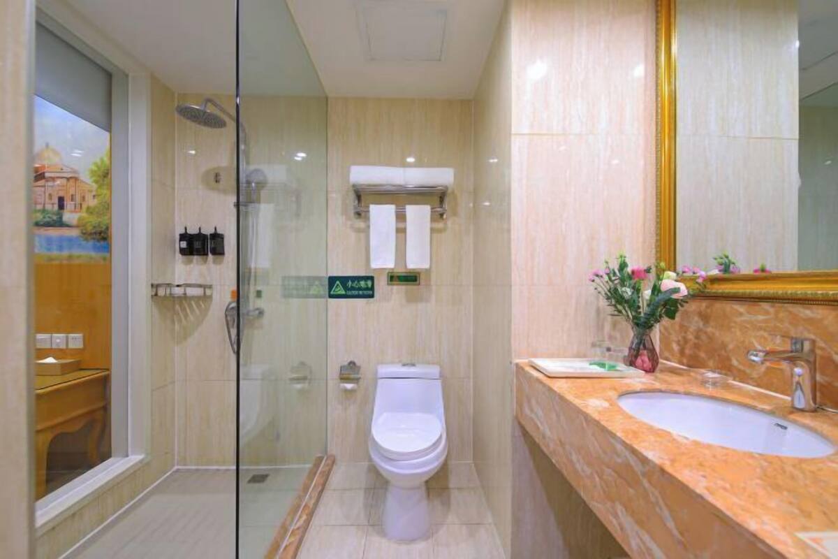 Un baño moderno con ducha de vidrio, inodoro blanco y lavamanos de mármol con un espejo grande.