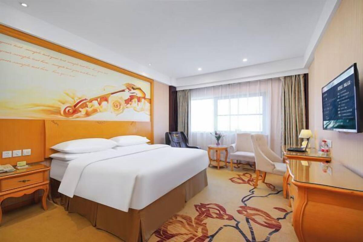Una habitación de hotel con una cama grande, un escritorio, una silla, una mesita y una televisión.