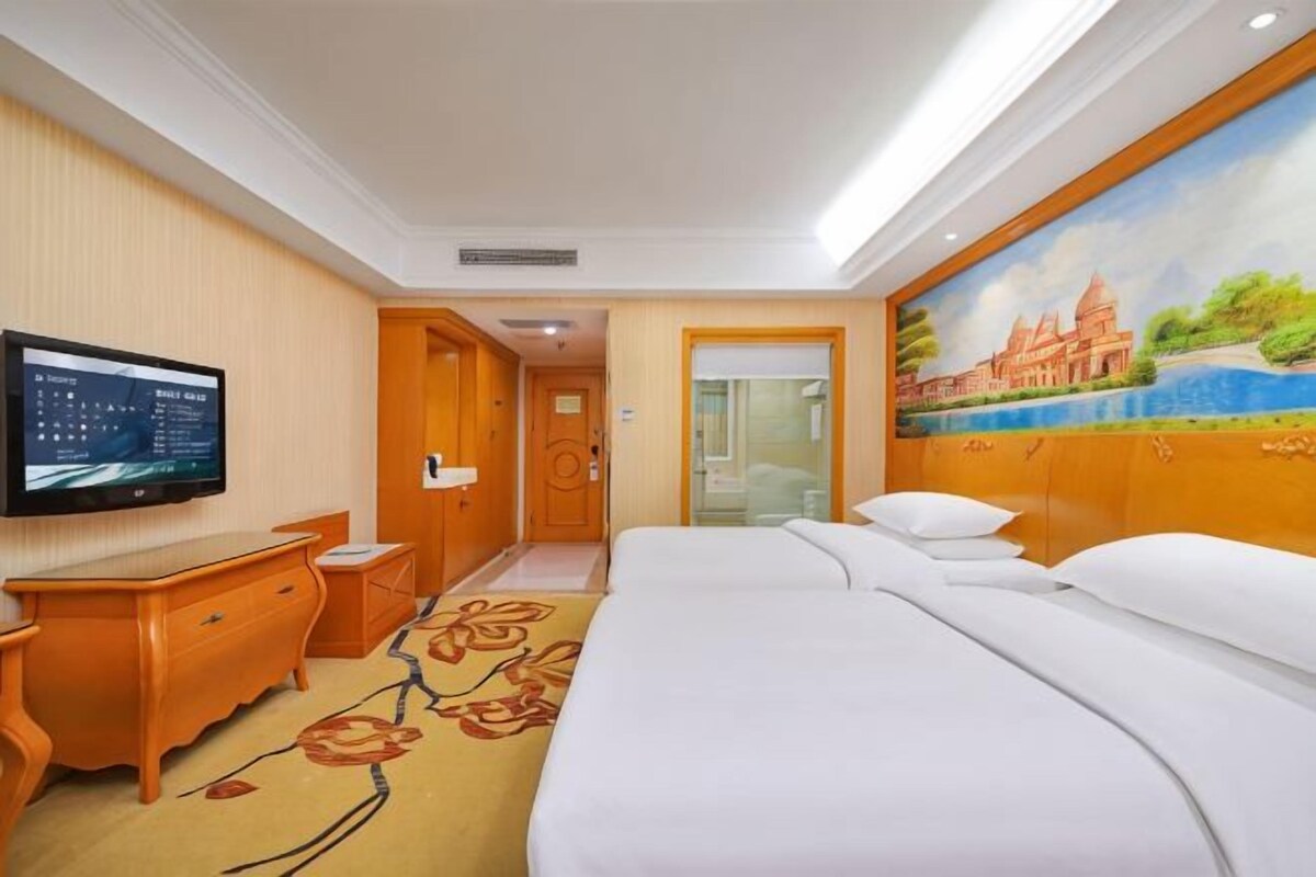 A hotel room with a bed, a television, a desk, and a painting on the wall.