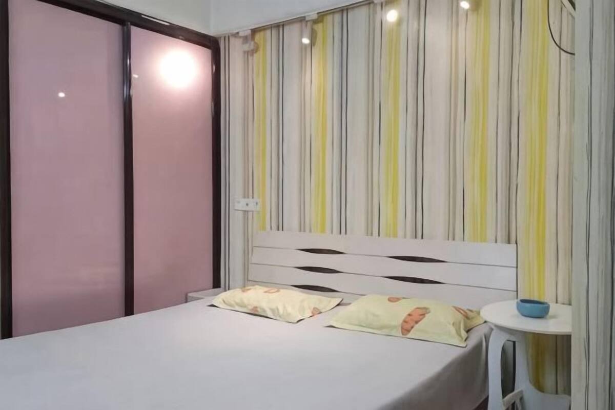 Ein Schlafzimmer mit einem Bett, einem Nachttisch, einem Kleiderschrank und einem gestreiften Vorhang.