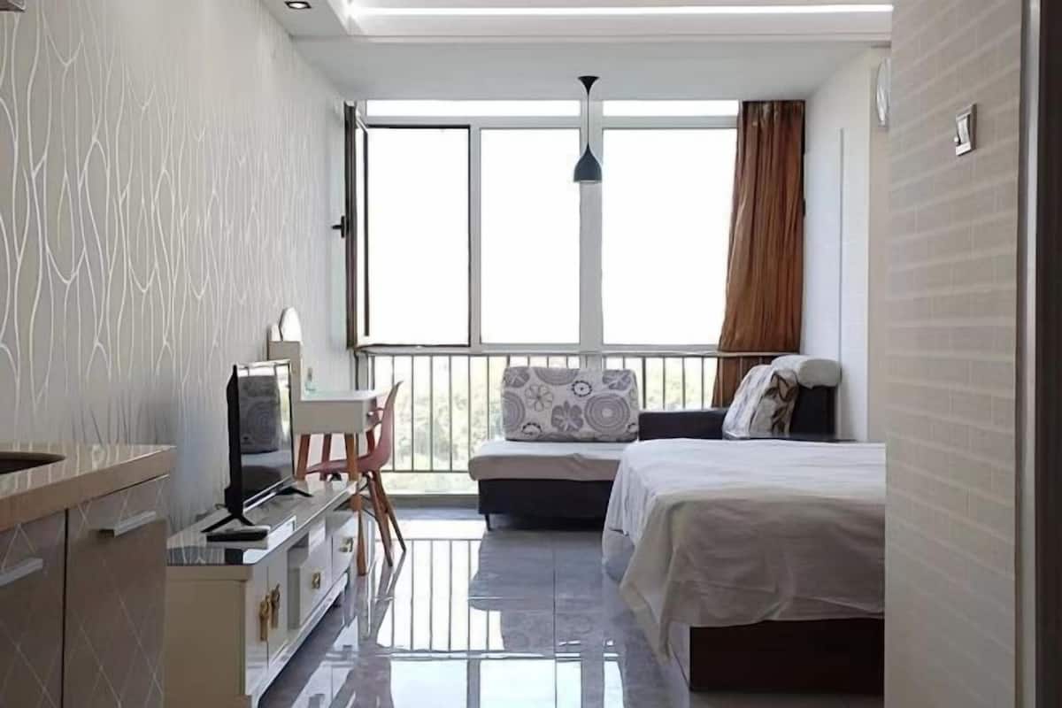Ein modernes Hotelzimmer mit einem Bett, einem Schreibtisch mit Computer, einem Sessel und einem großen Fenster mit Vorhängen.