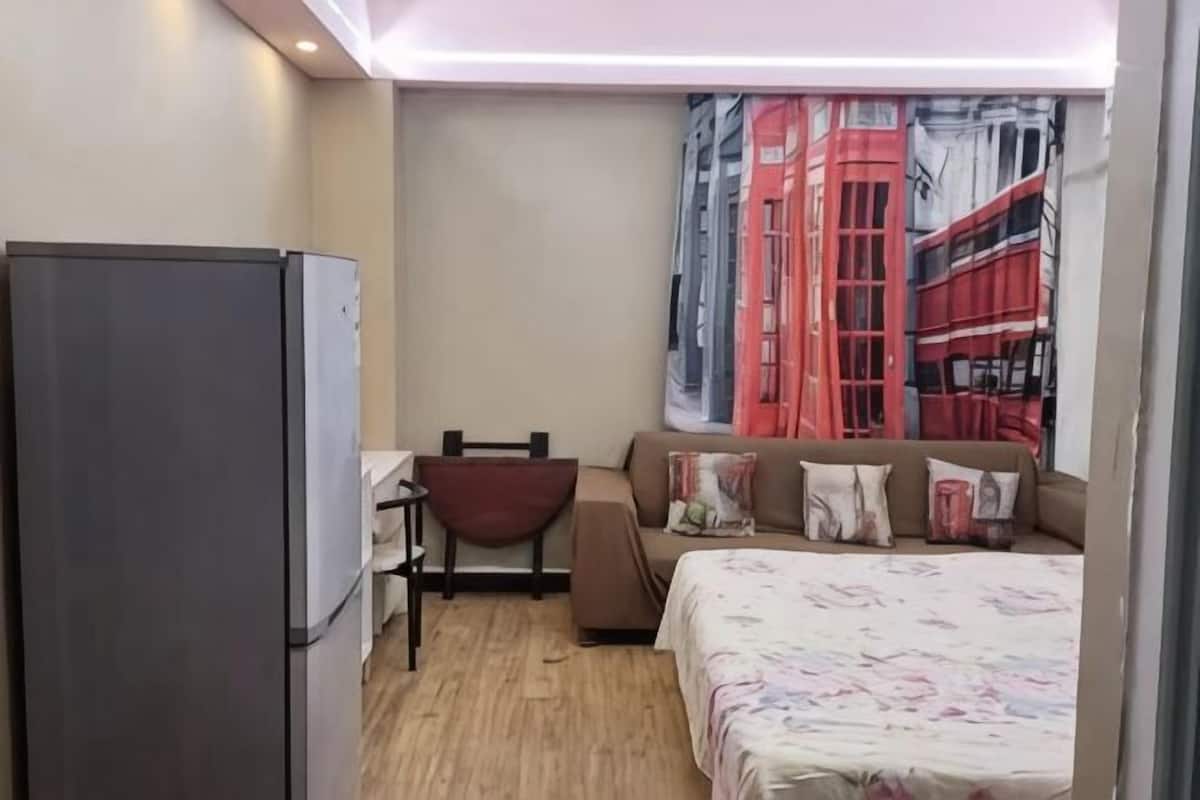 Ein kleines Hotelzimmer mit Bett, Schreibtisch, Stuhl, einer Couch und einem Kühlschrank.