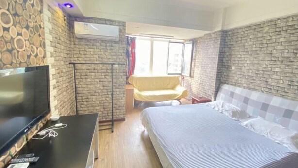 Un dormitorio con cama, televisión, escritorio con silla, ventana con cortinas y pared con diseño de piedra.