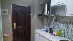 Una pequeña cocina con una puerta de madera oscura, armarios blancos, salpicadero de mármol y un lavamanos de acero inoxidable.