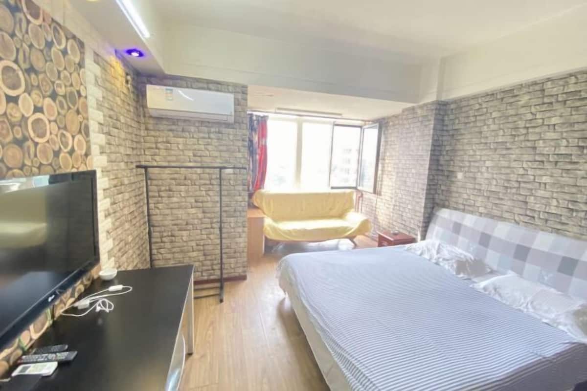 Ein Zimmer mit einem Bett, einem Fernseher, einem Sessel und einer Steinwand.