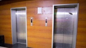 Dos puertas de ascensor en un vestíbulo con paneles de madera y suelo de baldosas.