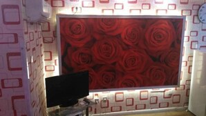 Una habitación con un amplio mural de rosas rojas, un televisor de pantalla plana sobre un soporte, y una pared decorada con diseños geométricos.