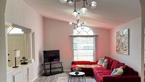 A living room with a red sofa, a TV, and a chandelier. - Updated luxury 4 Bed W/ KING Bed, FREE Heated Pool, Central Location (Port Charlotte)