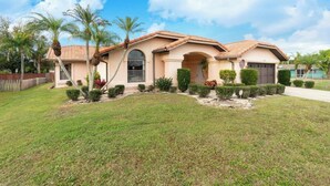 A two-story house with a tiled roof, a front porch, and a well-maintained lawn. - Updated luxury 4 Bed W/ KING Bed, FREE Heated Pool, Central Location (Port Charlotte)
